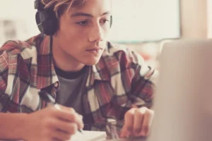 young, male college student wearing headphones and working at laptop