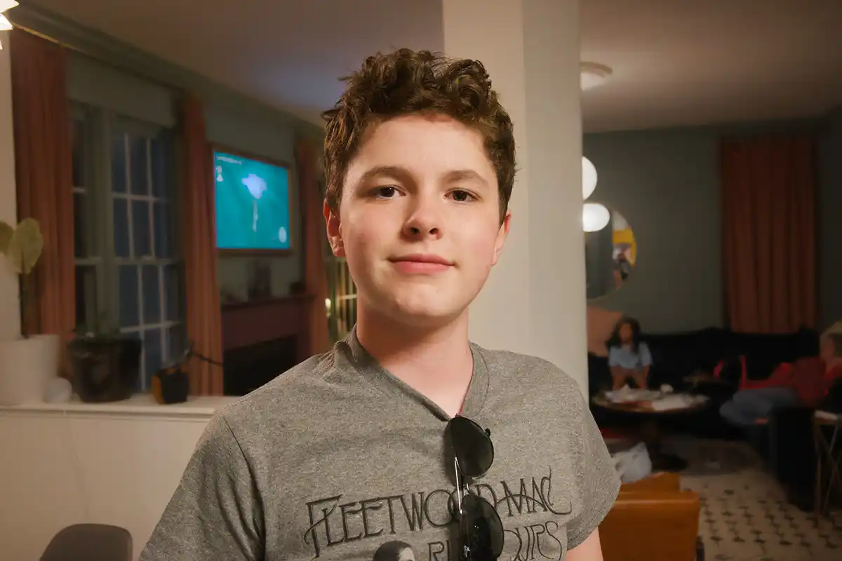 A twelve year-old boy smiles at the camera in his living room.