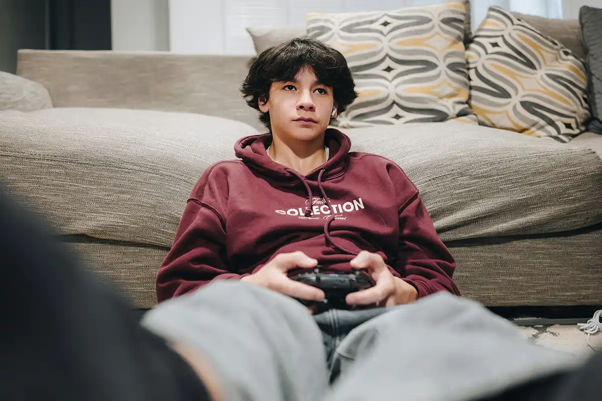 Teenage boy holds a gaming controller and stares off into the distance.