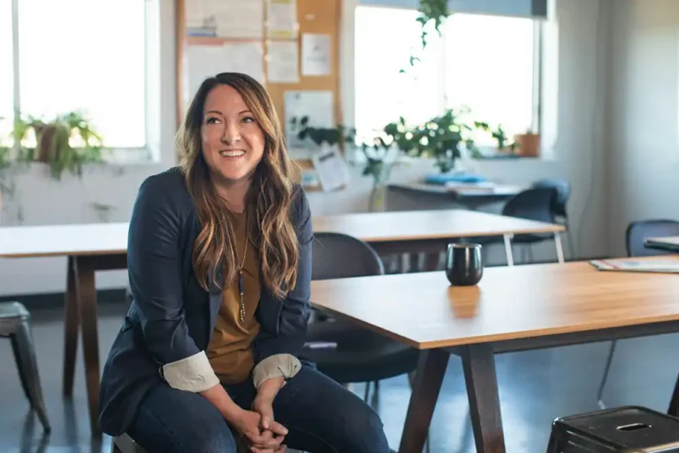 A thirty to forty-something woman sitting in a chair at work and smiling.